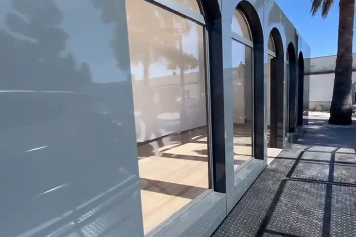 Caseta modular con fachada de panel y carpintería oscura en arco