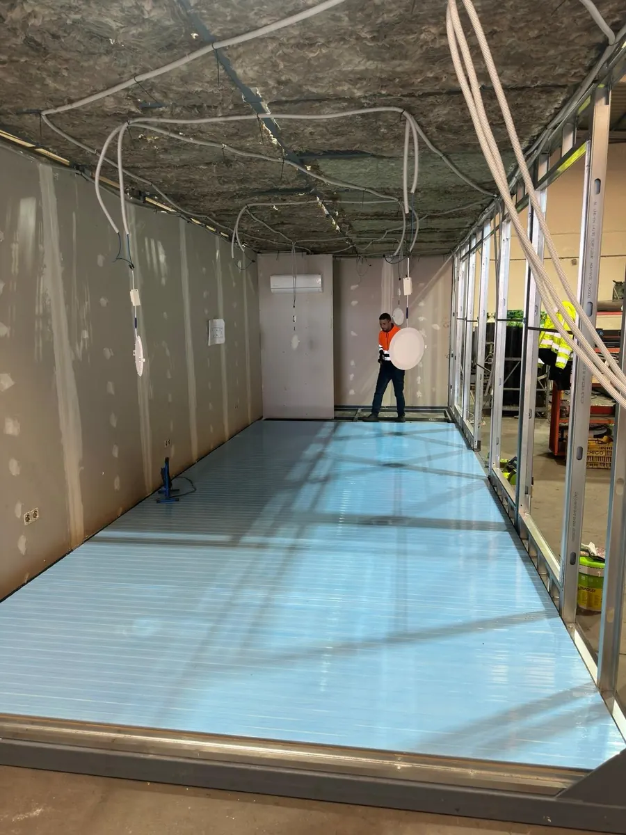 Interior de una caseta modular en fabricación: paredes y suelo ya colocados, con las instalaciones del techo a la vista