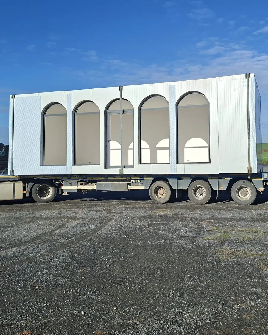 Caseta modular ECOMOD con ventanales en arco cargada en un camión, de camino a obra
